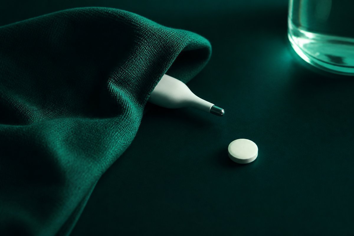 Forest-green still life: hidden thermometer under a cloth, tablet visible