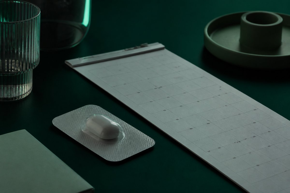 Forest-green still life: calendar length beside a DR capsule