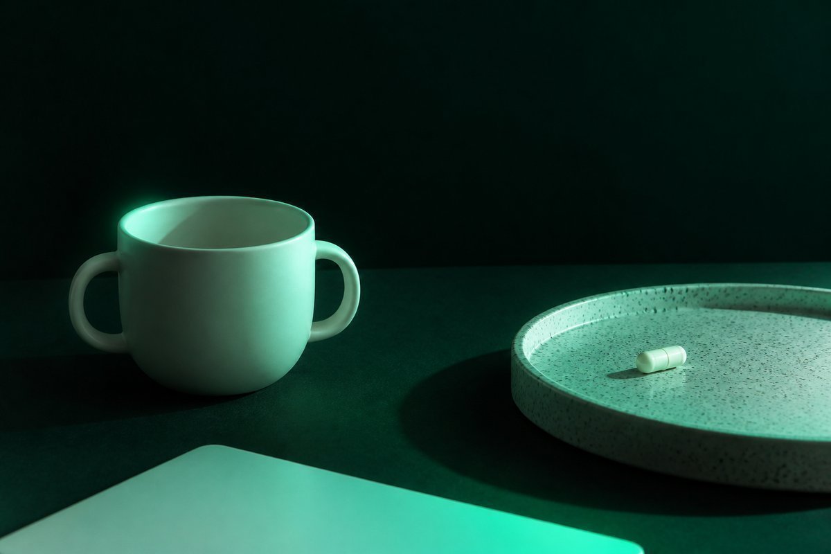 Forest-green still life: child cup empty, adult capsule only