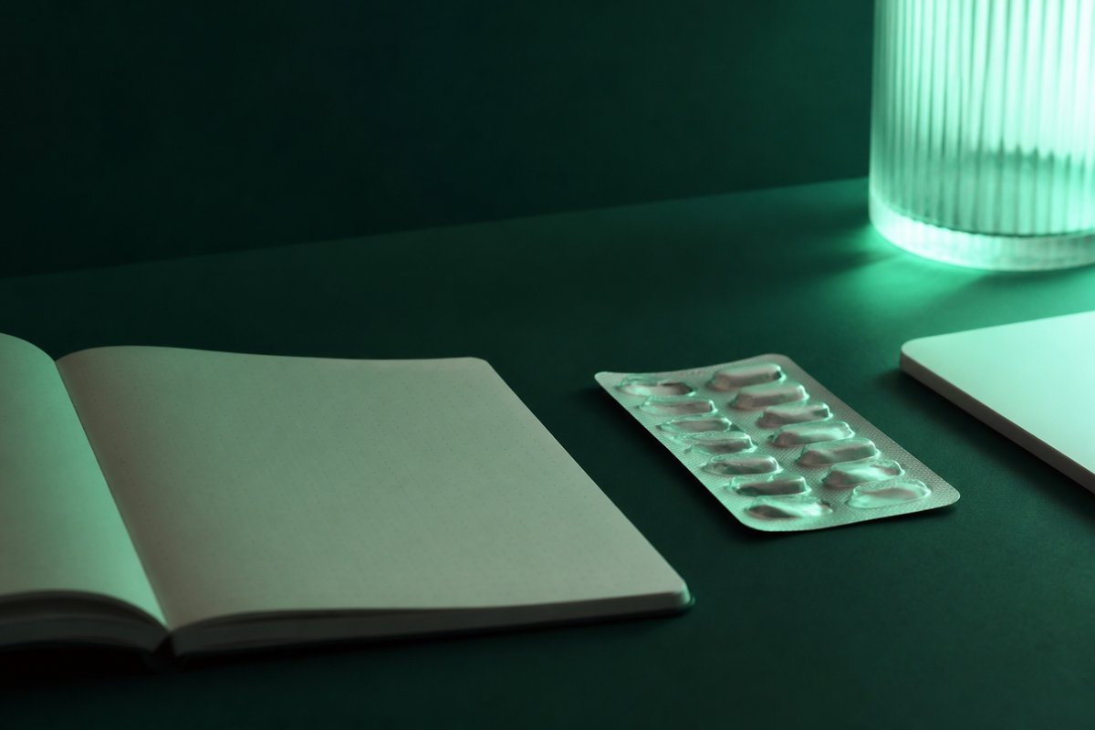 Forest-green still life: quiet notebook after a stop, empty blister