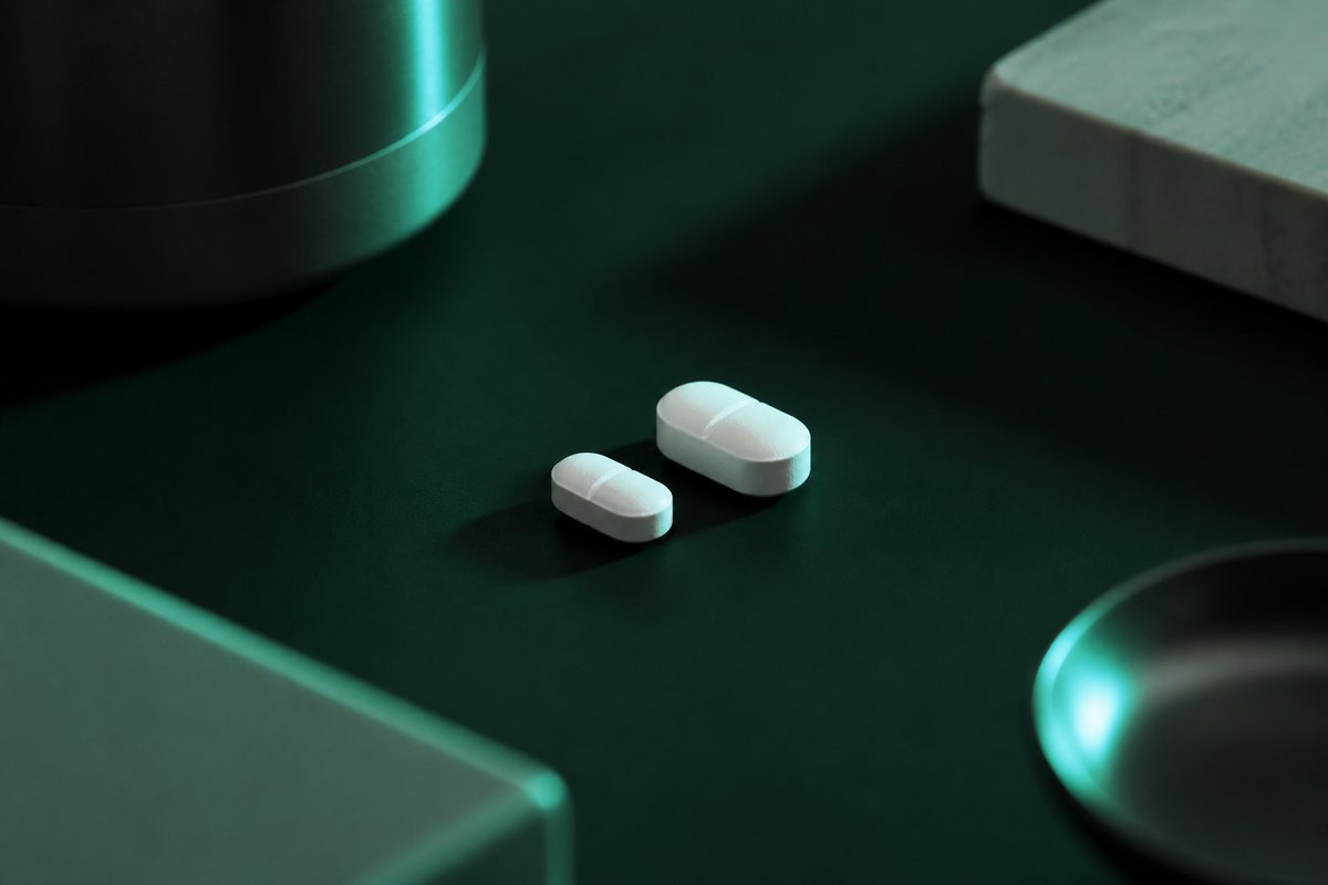 Forest-green still life: small white tablet beside a larger twin