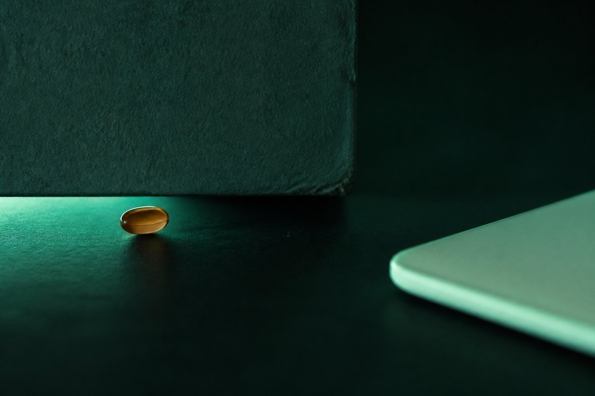 Forest-green still life: tiny amber tablet under a low ceiling mark