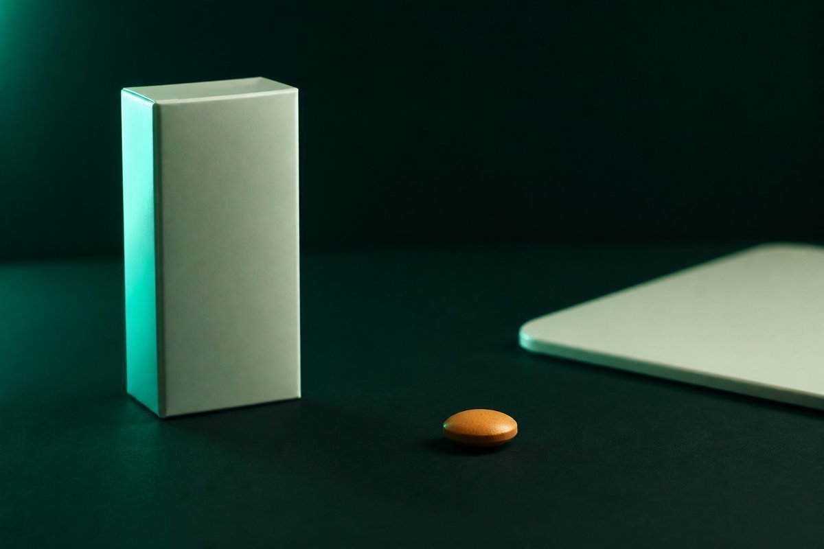 Forest-green still life: nitrate spray boxed away from an amber tablet