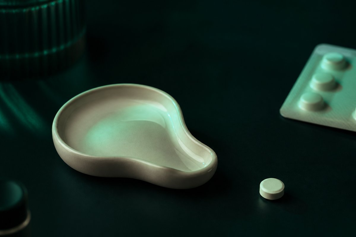 Forest-green still life: warm flush of mint light on a cheek-shaped ceramic, tablet aside